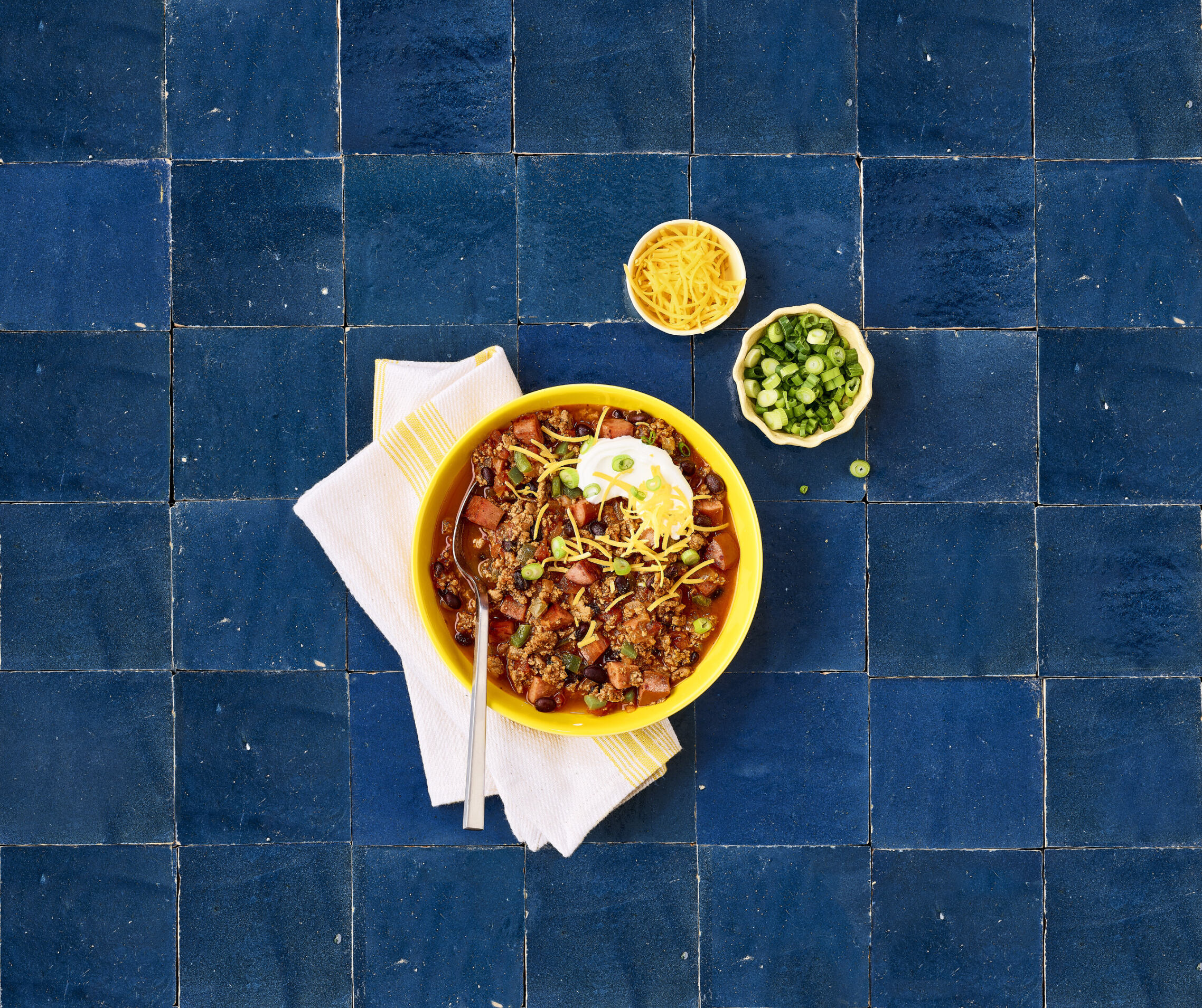 Chili in a bowl with two small side bowls on a blue tile table 