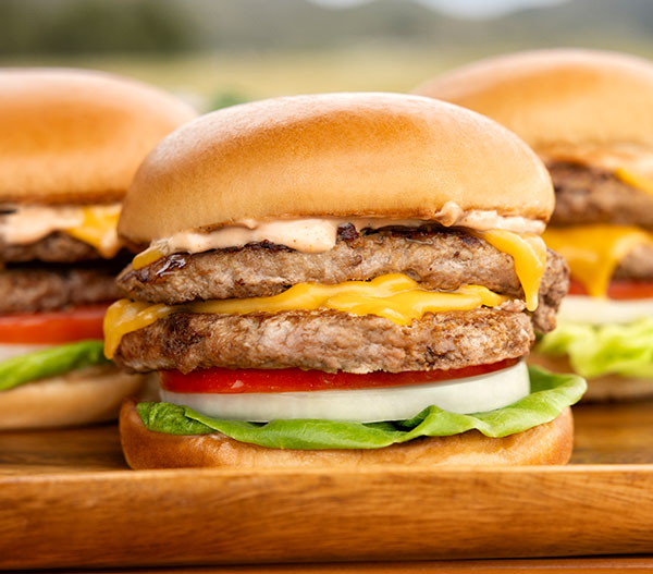 Stacked turkey cheeseburgers with lettuce, tomato, onion, and melted cheese on a soft bun.