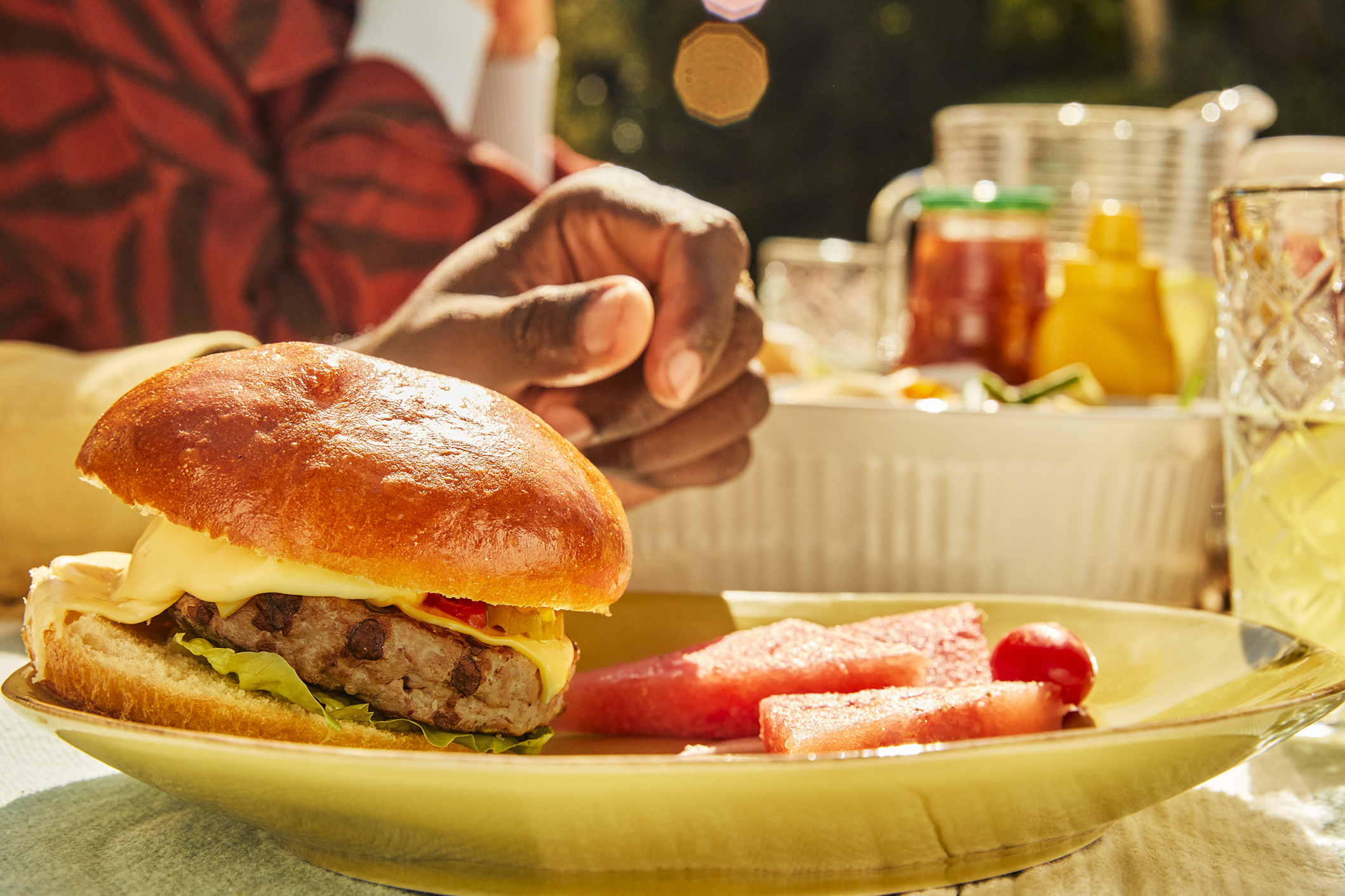 A burger and watermelon on a plate with picnic condiments in the background.