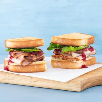 A turkey sandwich recipe with cranberry sauce, cheese, and lettuce on toasted bread, cut in half.