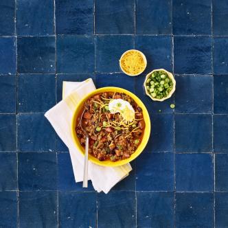 Chili in a bowl with two small side bowls on a blue tile table 