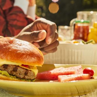 A burger and watermelon on a plate with picnic condiments in the background.