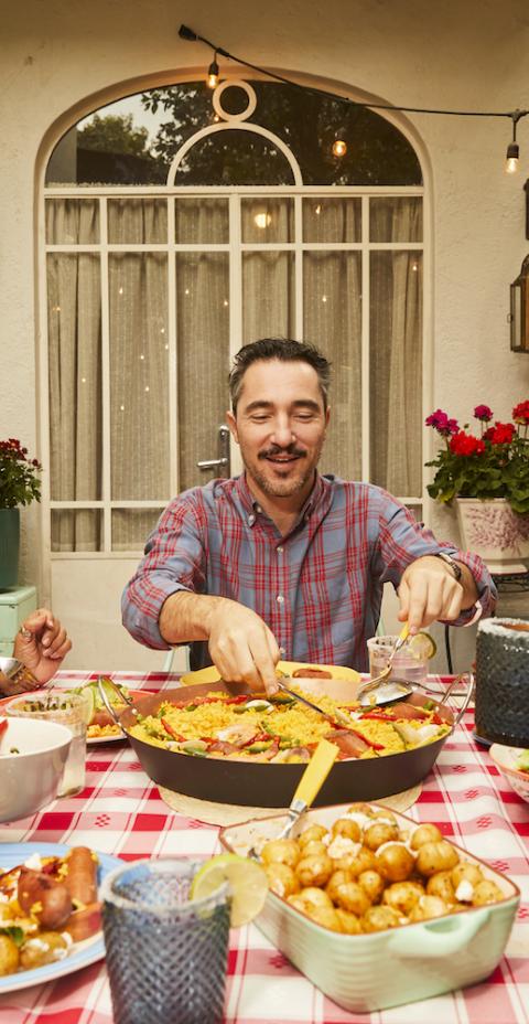 A group gathered outdoors sharing a meal with dishes like paella, potatoes, and vegetables.
