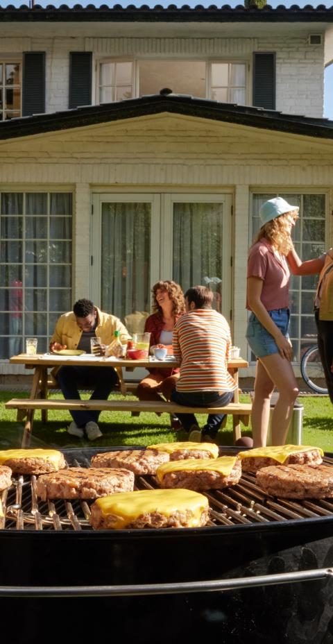 Friends enjoying a backyard barbecue with burgers on the grill.
