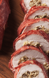 A Butterball Turkey Breast Tenderloin stuffed and wrapped with Butterball Turkey Bacon, sliced on a cutting board.