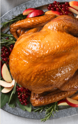 A roasted turkey on a metal platter with apple slices, berries, and thyme sprigs.