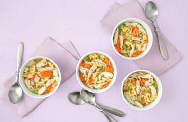 A comforting turkey soup recipe with egg noodles, carrots, and shredded turkey in white bowls.
