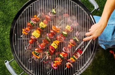 A person using tongs flips Butterball smoked sausage turkey kebabs on a grill.