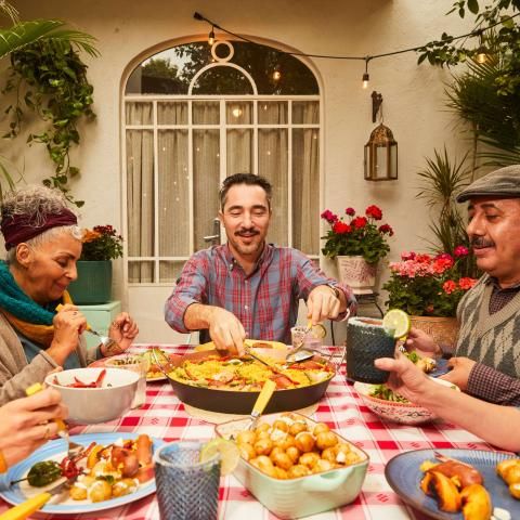 Family and friends gather around a large table enjoying paella.