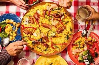 Paella with smoked turkey sausage, shrimp, clams, and veggies served on a red checkered tablecloth.