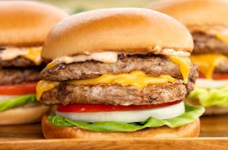 Stacked turkey cheeseburgers with lettuce, tomato, onion, and melted cheese on a soft bun.