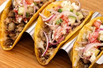 Turkey crispy tacos topped with veggies, onions, and cheese, served on a tray for a tasty meal.