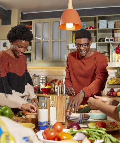 Family talking and laughing in the kitchen while preparing a meal.