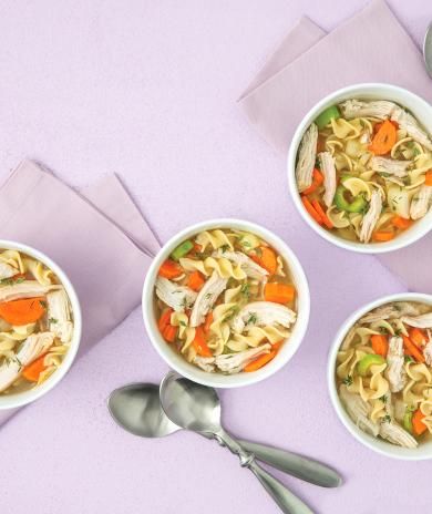 A comforting turkey soup recipe with egg noodles, carrots, and shredded turkey in white bowls.