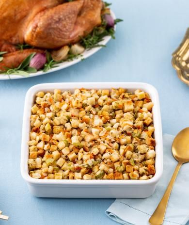 Classic turkey stuffing recipe in a white baking dish, with a roast turkey in the background. 
