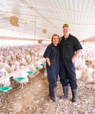 Smiling farmers in a large turkey barn, dedicated to animal care and well-being
