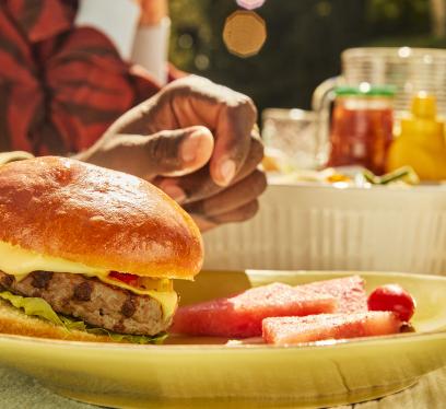 Turkey burger with cheese and watermelon slices on a plate at an outdoor summer cookout.