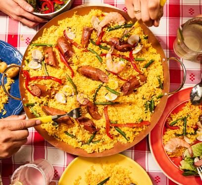 Paella with smoked turkey sausage, shrimp, clams, and veggies served on a red checkered tablecloth.