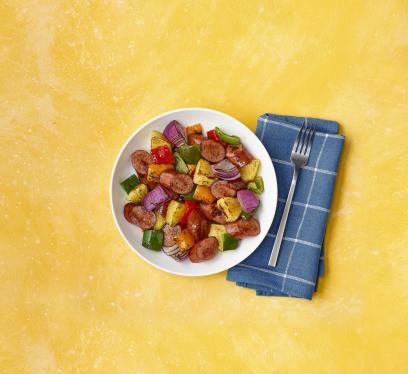 Bowl of turkey sausage, pineapple, peppers, and onions on yellow background with a blue napkin.