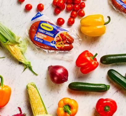 Two packs of Butterball Hardwood Smoked Turkey Dinner Sausage on a counter next to a variety of vegetables.