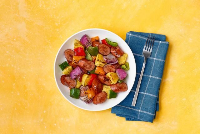 Bowl of turkey sausage, pineapple, peppers, and onions on yellow background with a blue napkin.