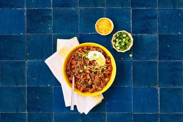 Turkey chili recipe in a yellow bowl, topped with sour cream, cheese, and green onions.