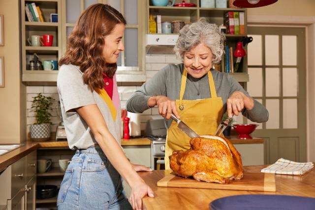 Passing down a family tradition as two generations prepare a roasted turkey for a shared meal.