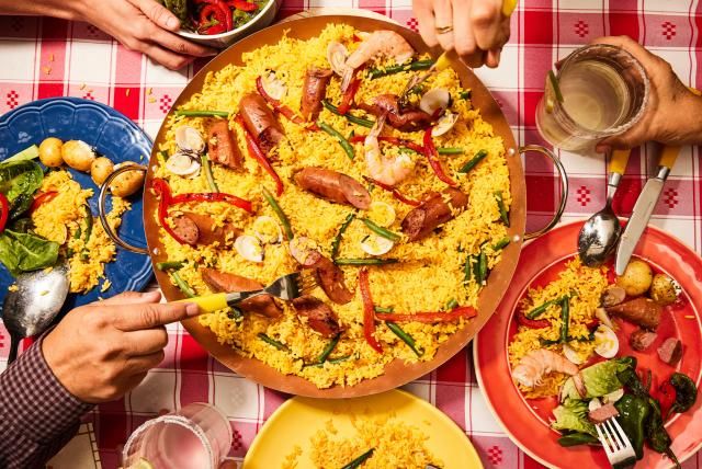 Paella with smoked turkey sausage, shrimp, clams, and veggies served on a red checkered tablecloth.
