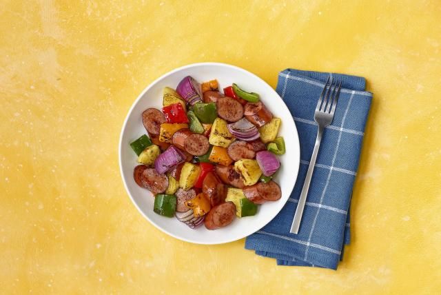 Bowl of turkey sausage, pineapple, peppers, and onions on yellow background with a blue napkin.