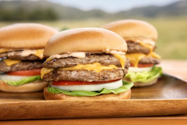 Three Butterball turkey cheeseburgers with lettuce, tomato, and onion served on a wooden tray.