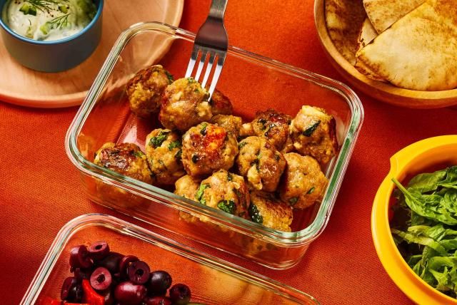 A person removes a Greek ground turkey meatball from a storage container with a fork.