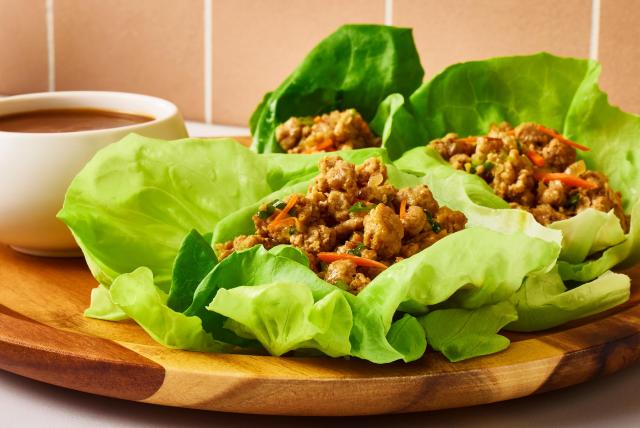 Butterball Thai ground turkey lettuce wraps on a plate next to a bowl of sauce.